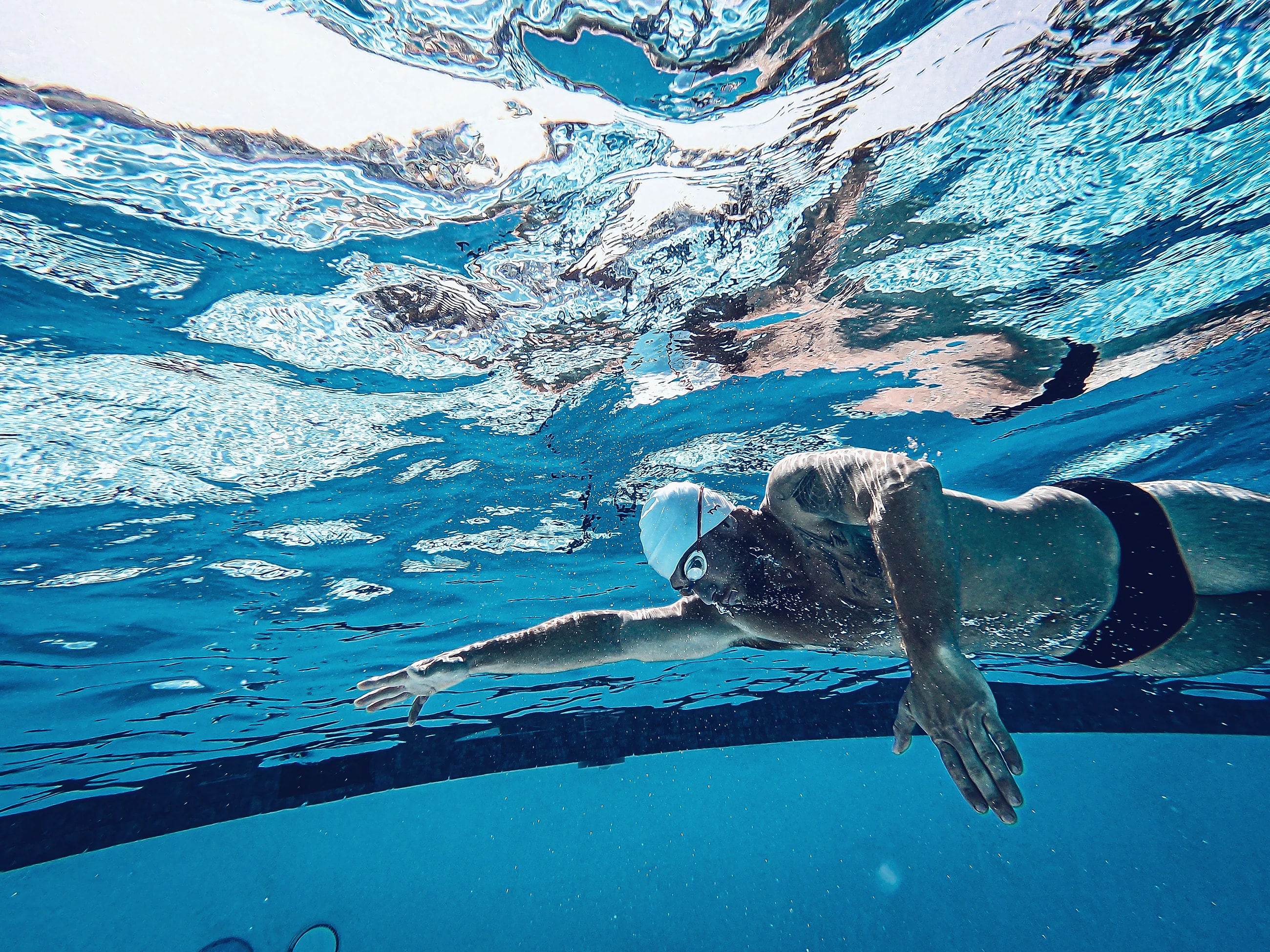 A swimmer gliding underwater, stretched long above the lane lines of a dark blue pool.