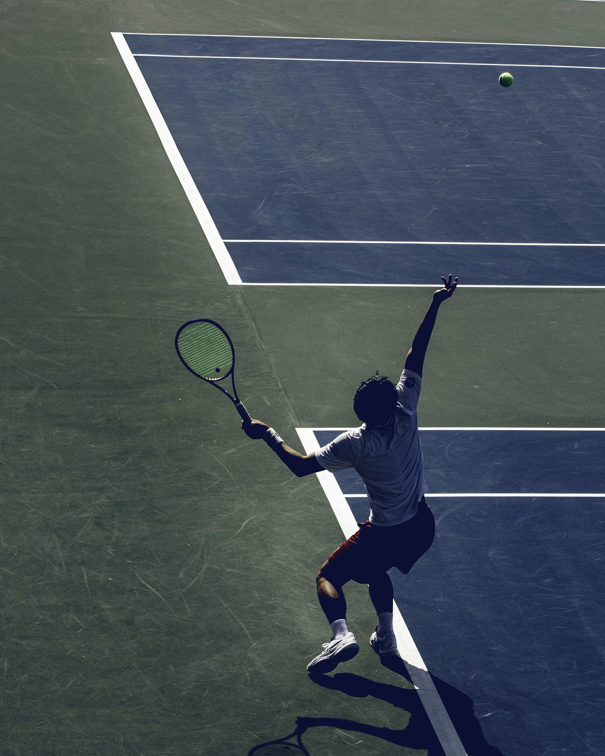 A tennis player’s hand releasing the ball for a serve, white court lines crossing a blue court.