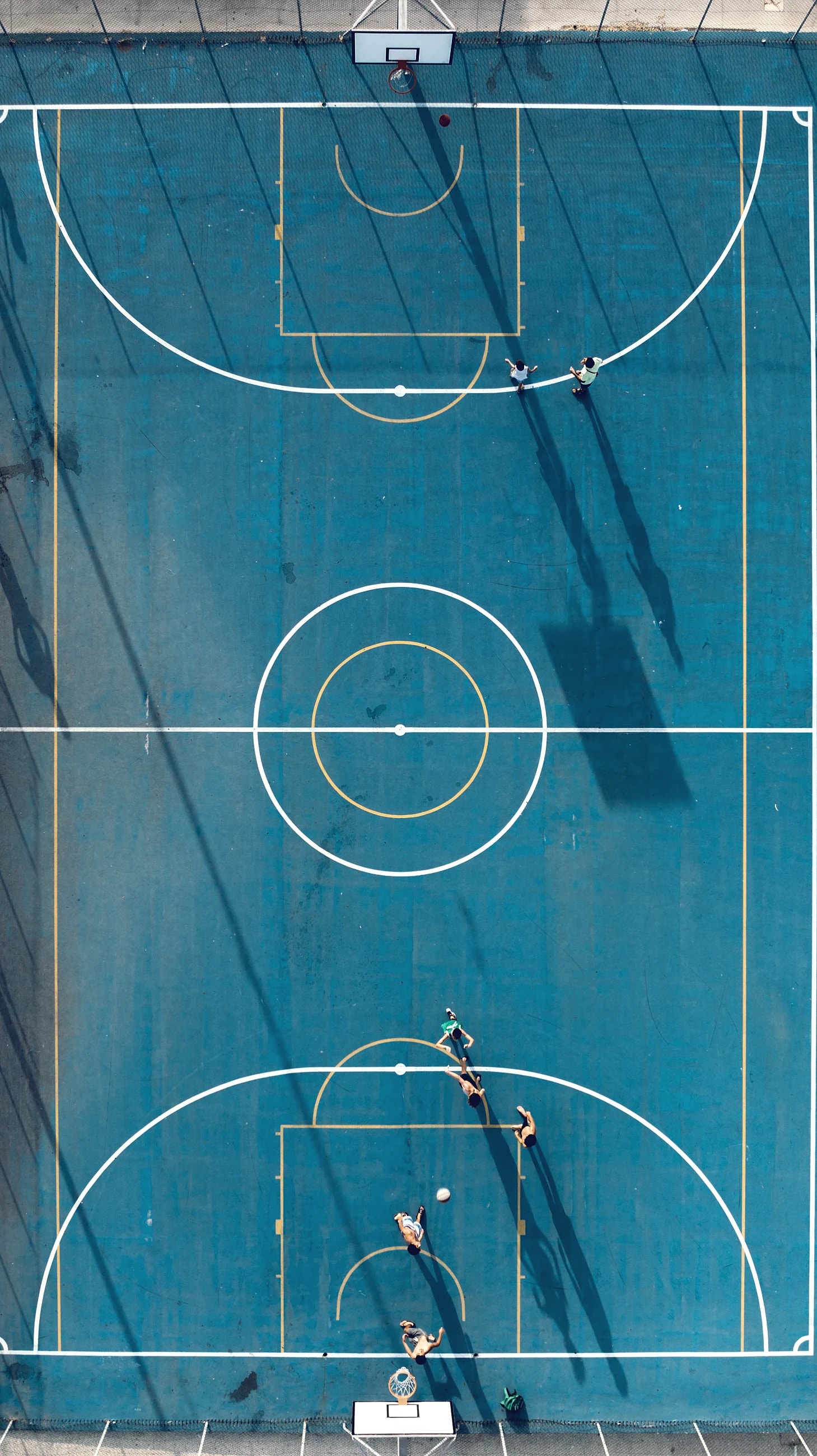A basketball court seen from directly above, its lines bright against a dark floor.