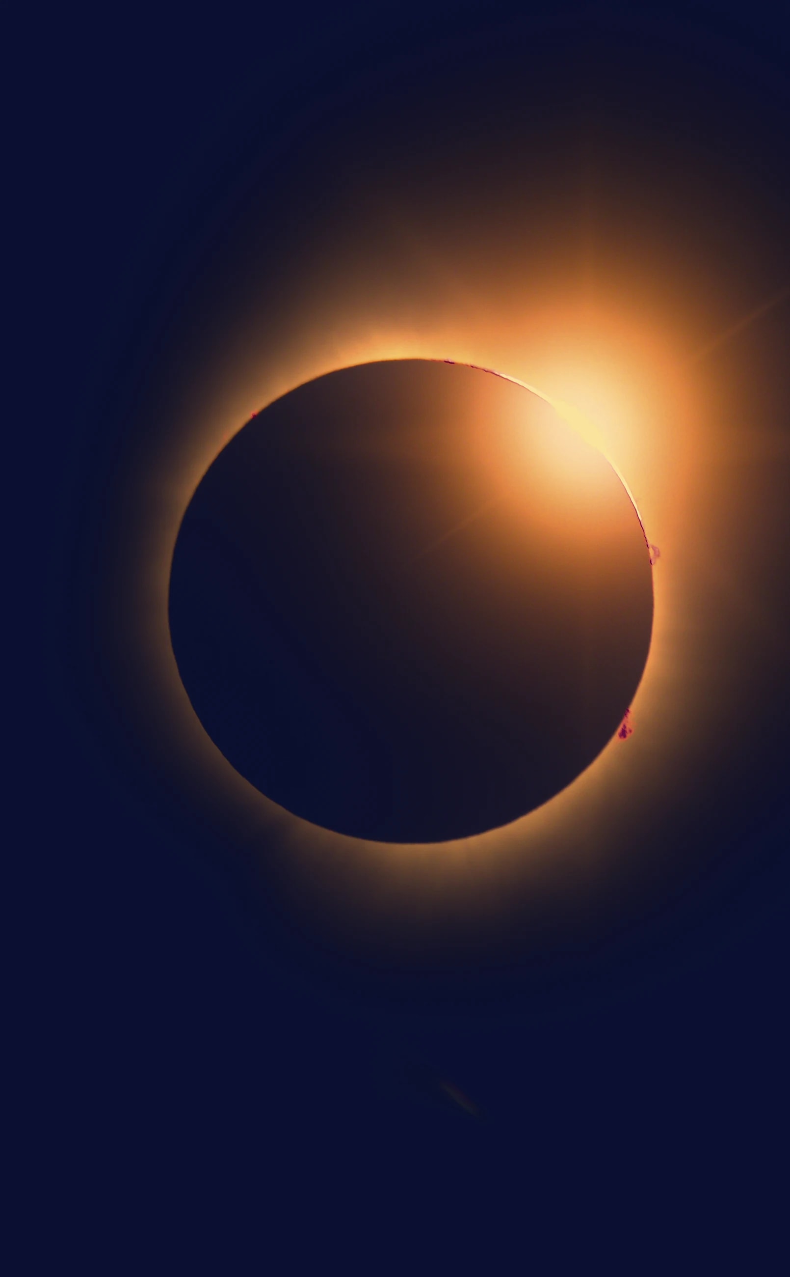 A solar eclipse: a dark disc ringed with red and orange light on a midnight sky.
