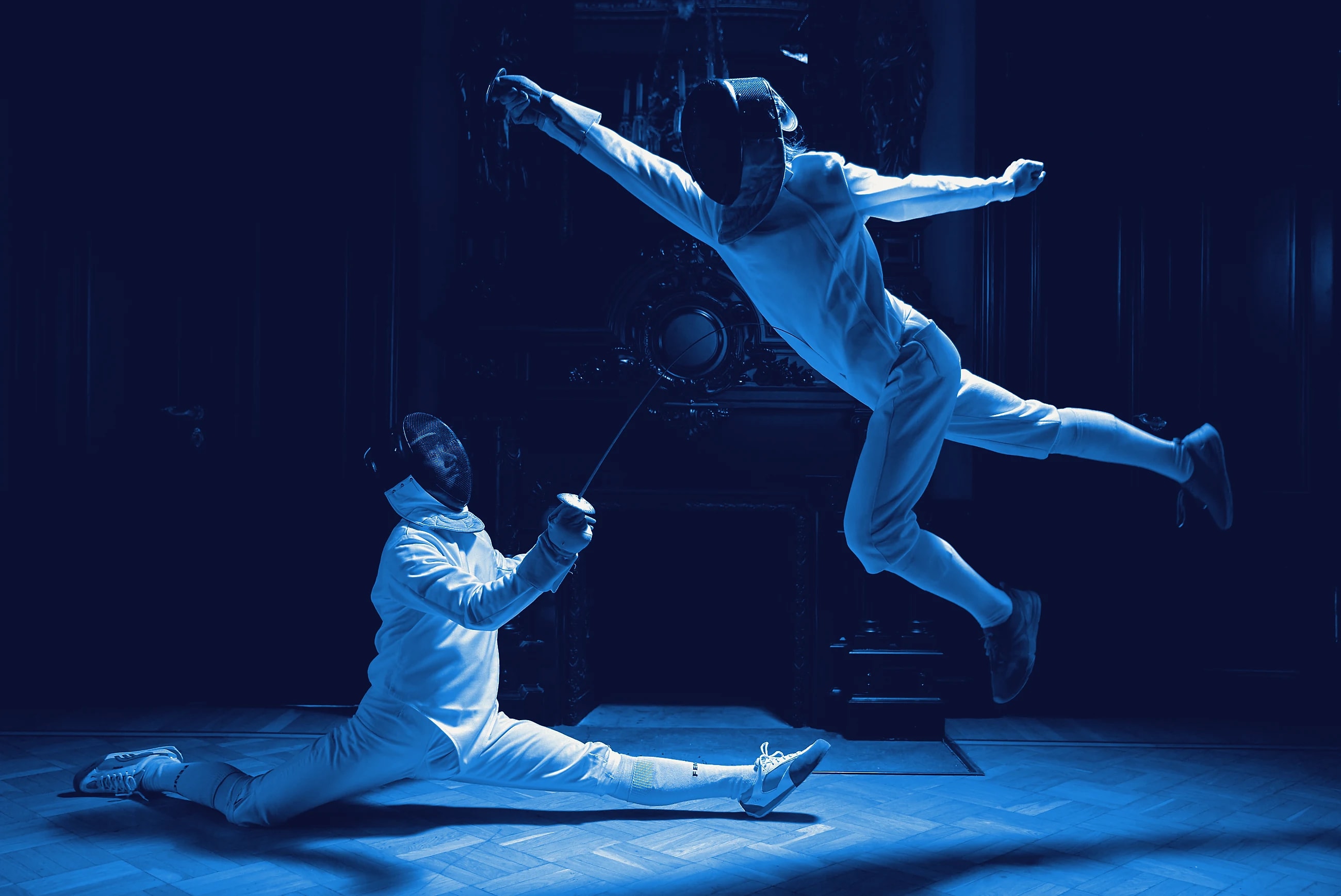 Two fencers in white mid-bout on a lit piste, one lunging forward.