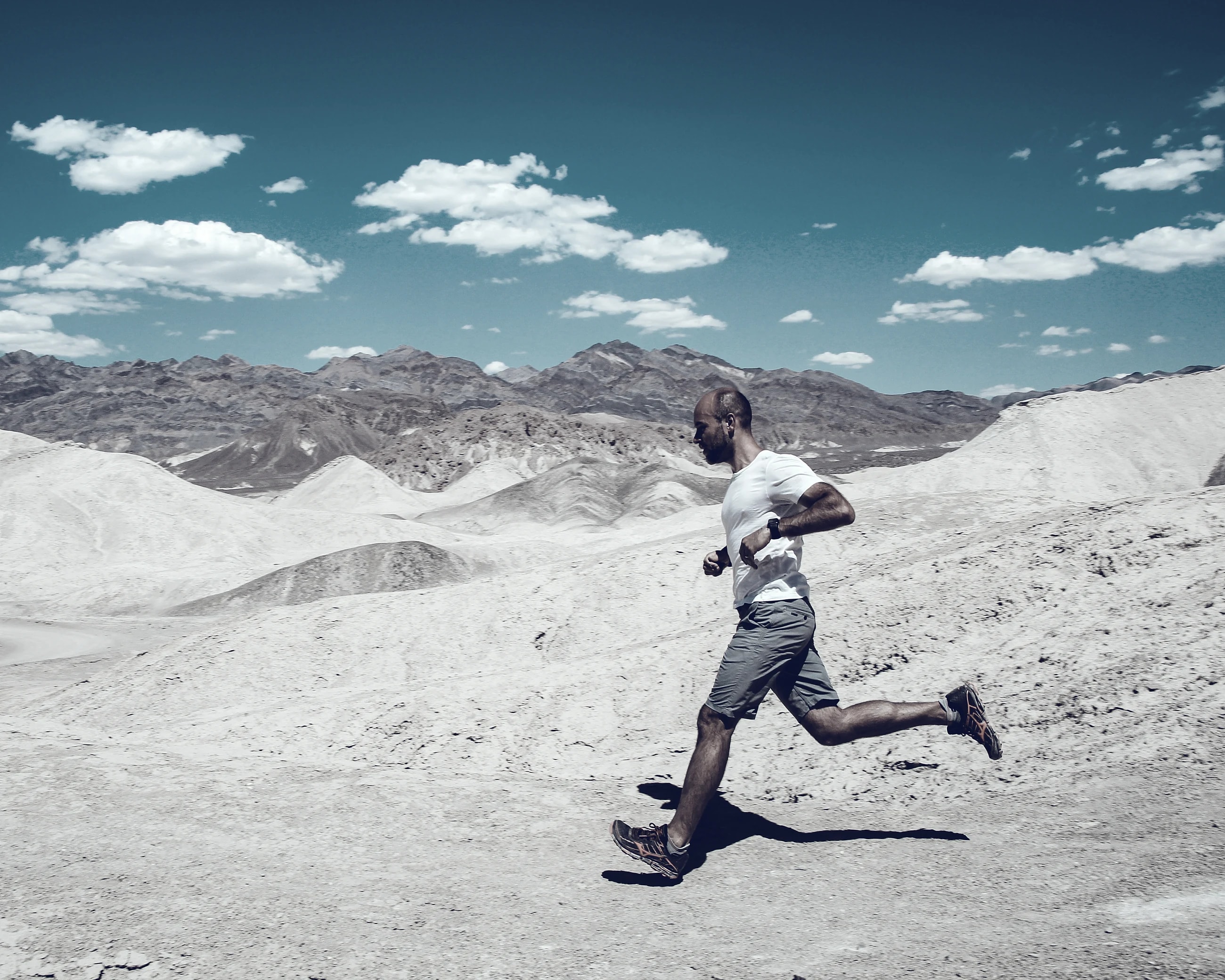 A lone runner crossing the pale chalk rock formations of a white desert under a bright sky.